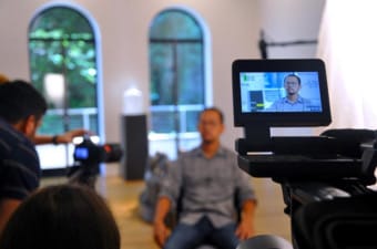 Brian Doan is seated for an interview as a camera focuses in on him. 