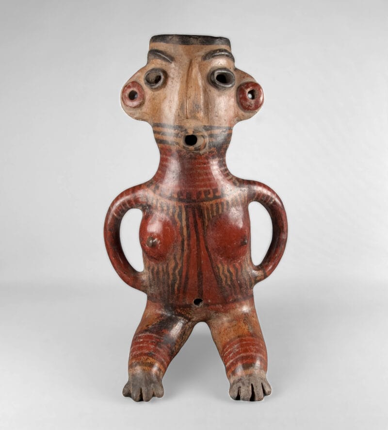 Stylized sculpture depicting a seated woman with hands on her hips, an open mouth, ear spools, and body paint.