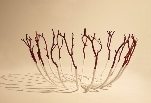 An off-white bowl made of steel prongs and dark red twigs.