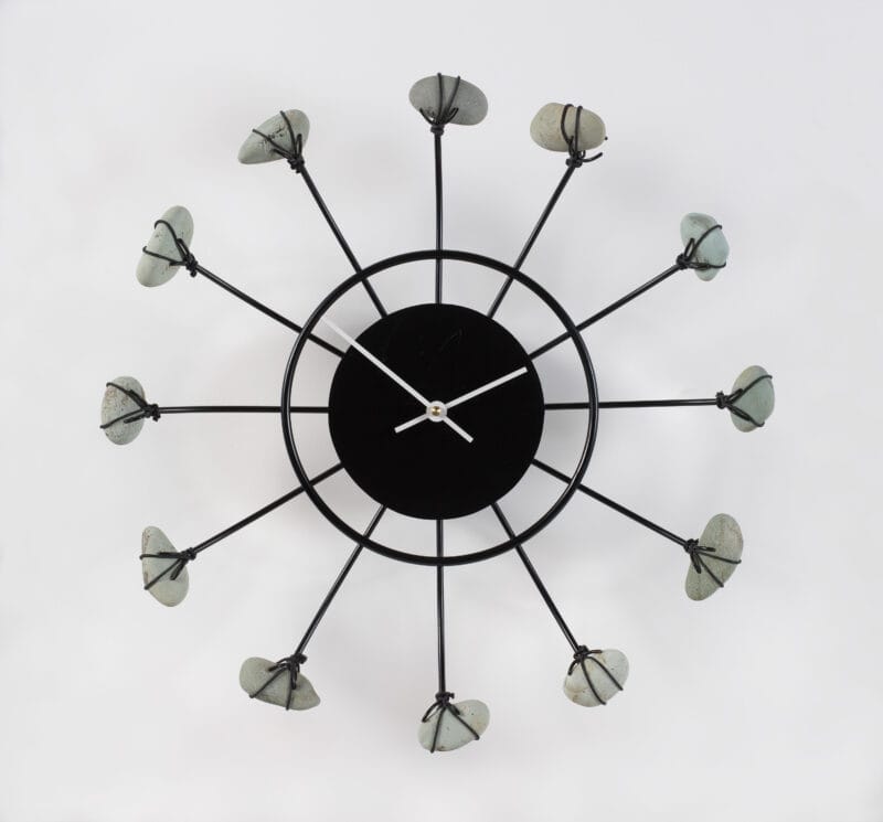 A black metal wall clock with gray stones depicting the hours.