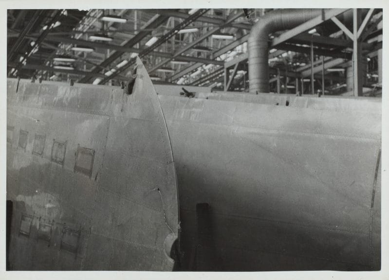 Black and white photograph of two aircraft wings lined up inside a factory.