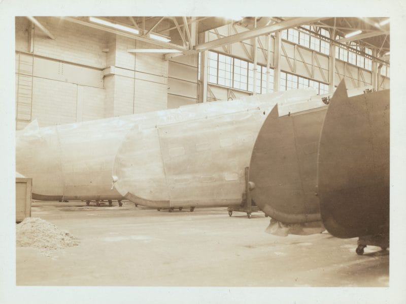 Sepia photograph of four aircraft wings lined up inside a factory.