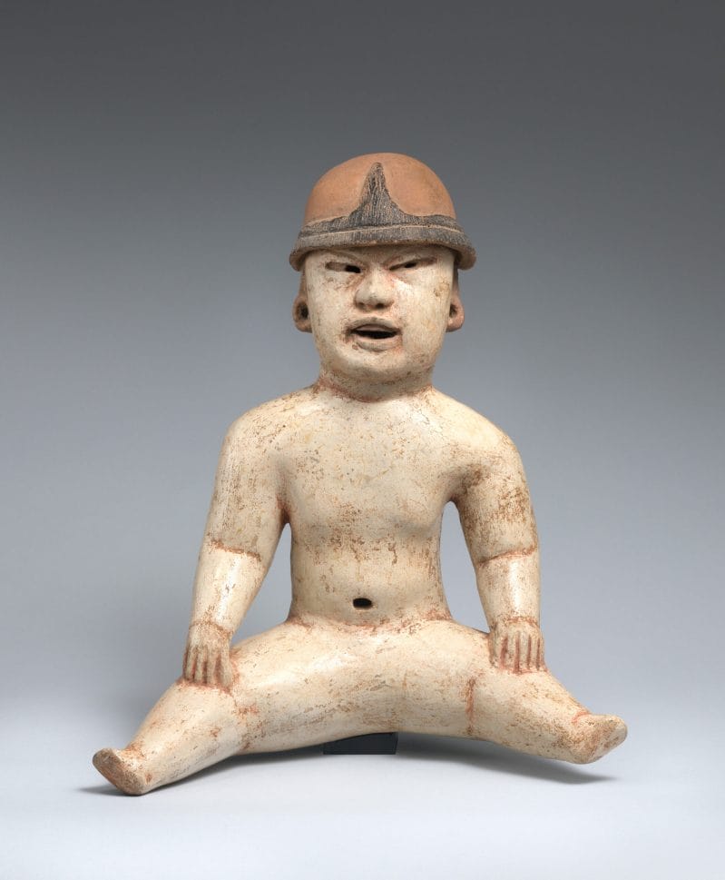 Ceramic seated figure of a baby with a white round body, open mouth, and red head covering.