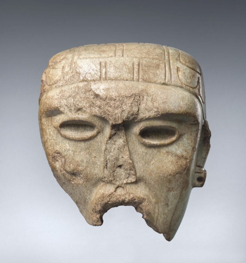Fragment of a stone mask with hollow eyes and an intricate headdress.