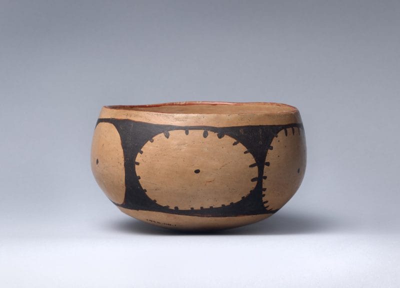 Clay pottery bowl with red rim and circular decorative shapes.