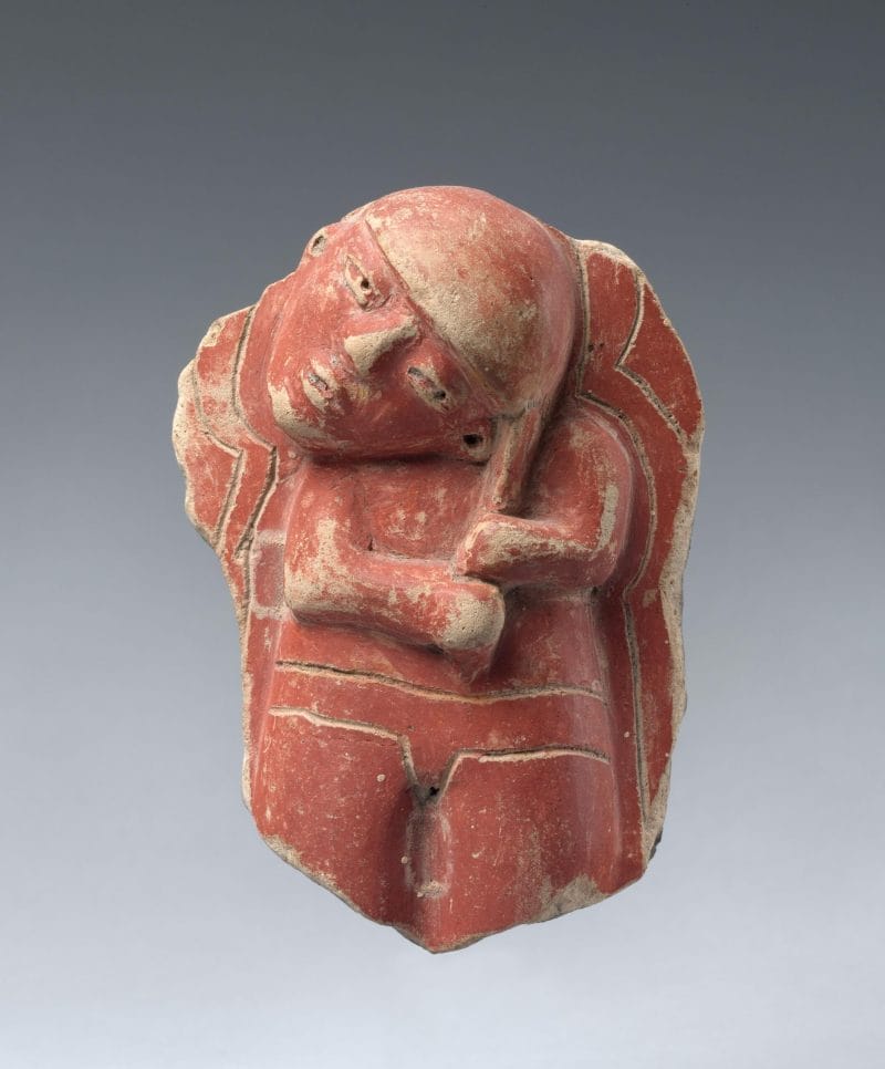 Ceramic fragment of a figure with a tilted head, painted in red.