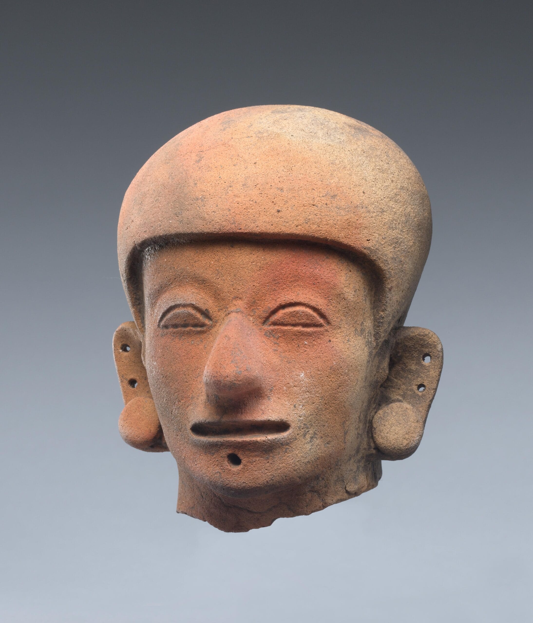 Ceramic human head wearing a helmet and ear spools.