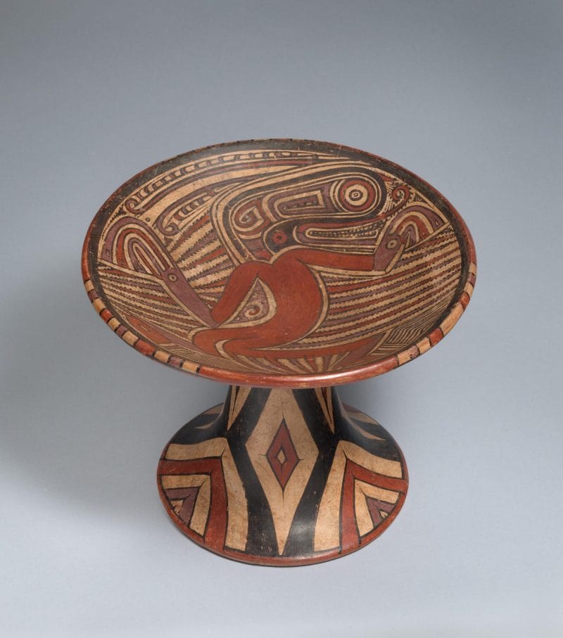 Pedestal plate with human and crocodile figures surrounded by patterns with geometric designs the on the base.