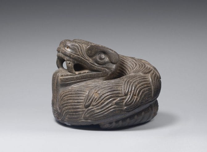 Sculpture of a coiled quetzalcoatl feathered serpent with open mouth exposing prominent fangs.