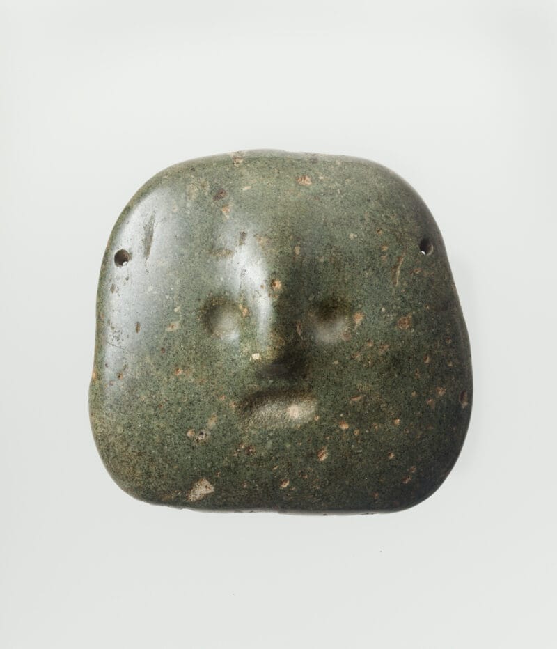 A round abstract stone mask with small indented eyes, mouth and a round nose.