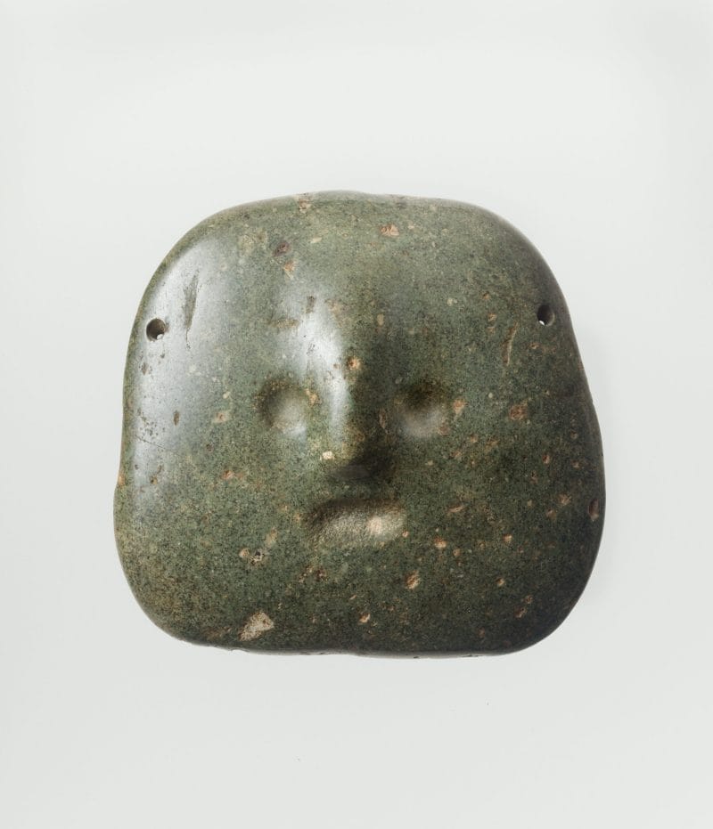 A round abstract stone mask with small indented eyes, mouth and a round nose.