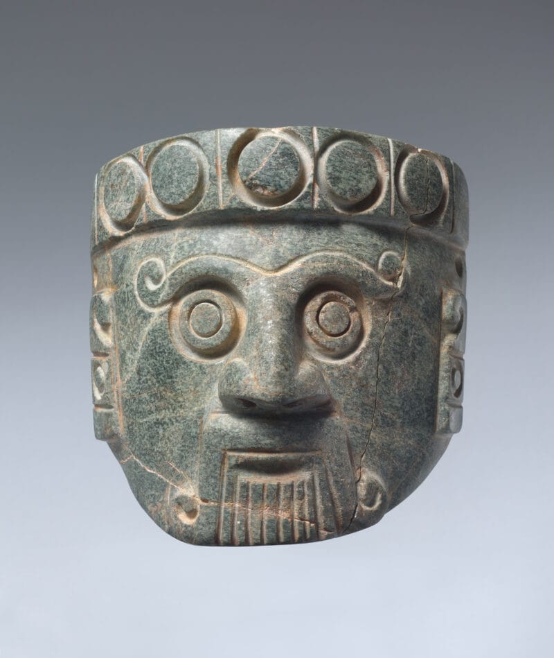 Stone head of a rain god with large bulging eyes and long fangs emerging from curled lips.