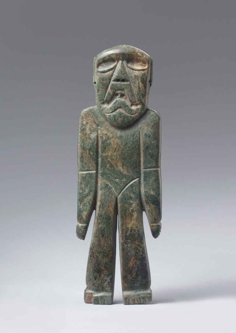 Standing stone figure with large eyes, triangular face, and hands resting at the sides.