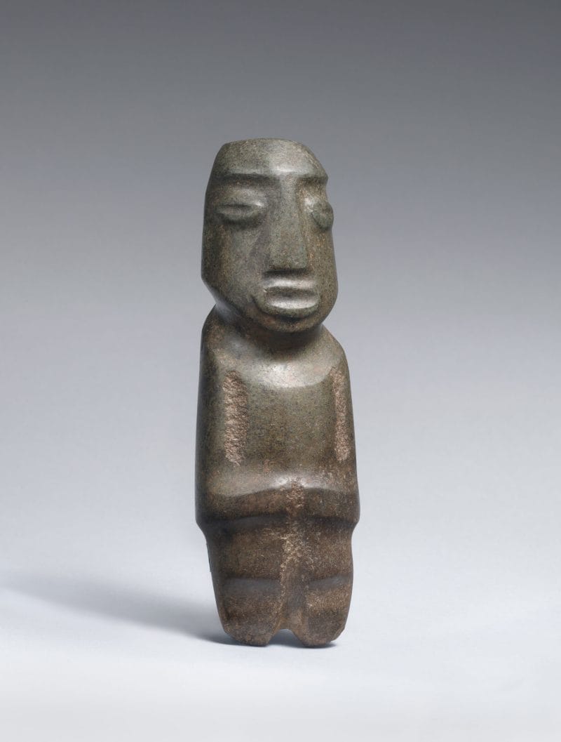 Small abstract stone scultpture with protruding facial features including eyes, mouth, and a flat geometric nose.