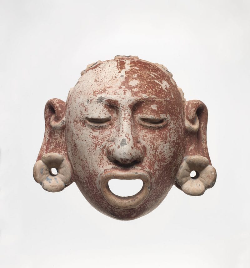 Decorative stone mask of an Aztec god with open mouth, closed eyes, and large pierced ears.