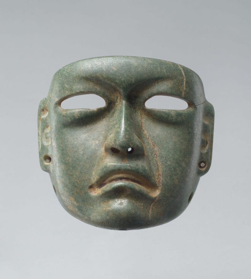 A mask with naturalistic features, including an open mouth, carved-out eyes, and spool holes in the nose and ears.