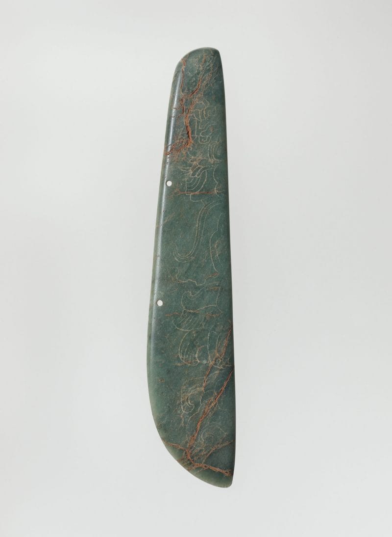 Pendant-like sculpture with engraved figures in elaborate feather headdresses and flowing garments.