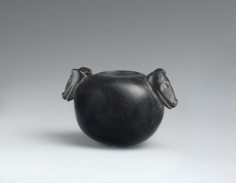 Polished vessel with stylized carving of identical canine heads on each side.