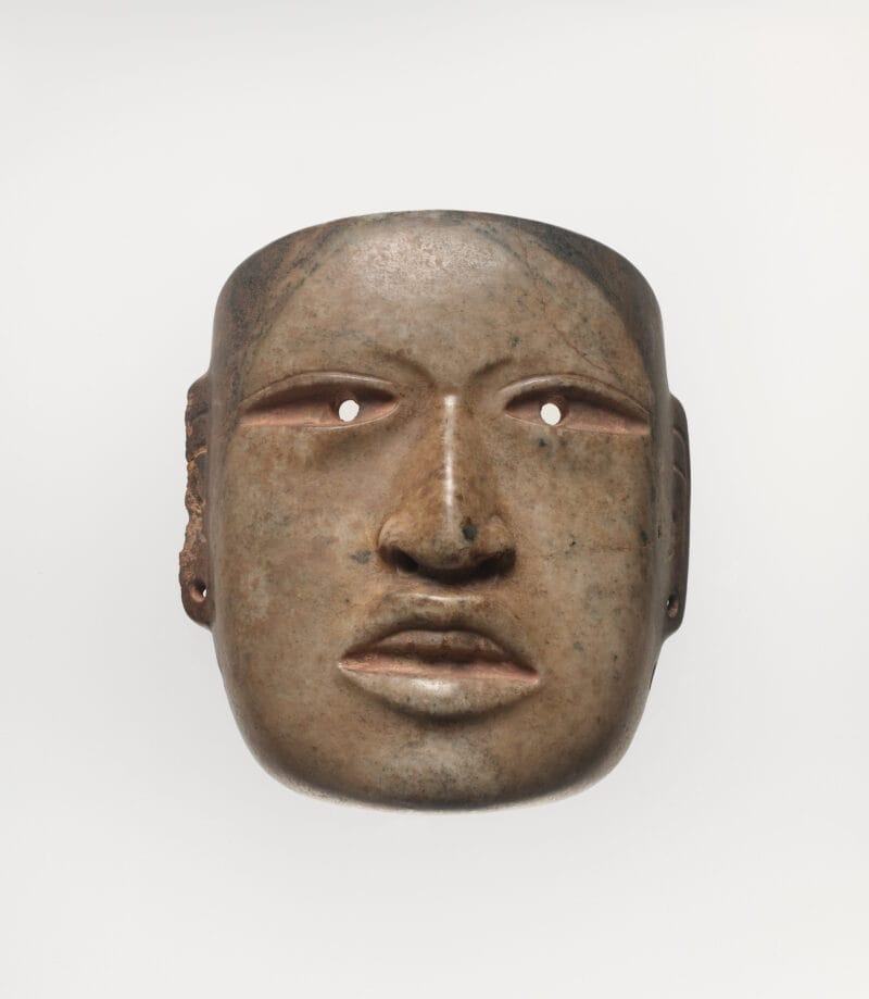 Ritualistic face mask with drilled eyes and ear spools, and a naturalistic mouth open to expose top teeth.