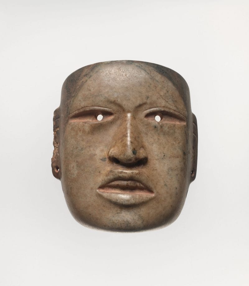 Ritualistic face mask with drilled eyes and ear spools, and a naturalistic mouth open to expose top teeth.