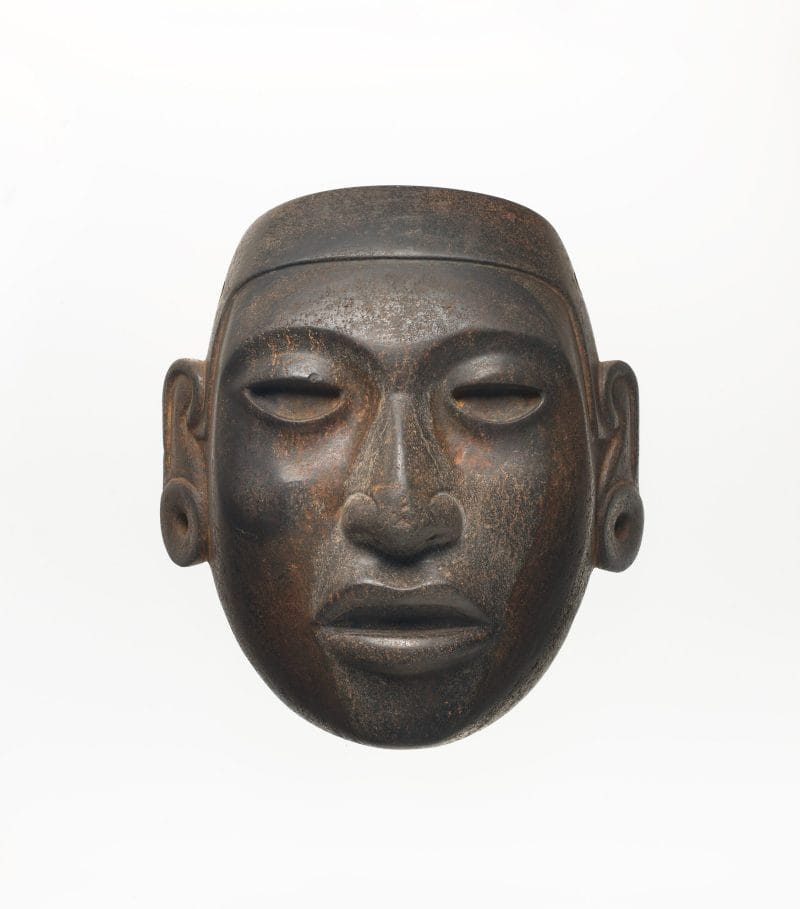 A brown mask with hollow eyes, a realistic mouth and nose, and pierced ear spools.