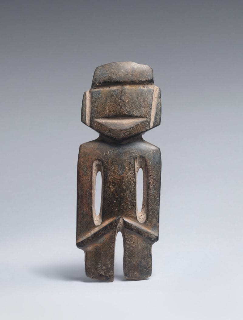 Brown stone figure with geometric cuts and hollows indicating physical and facial features.