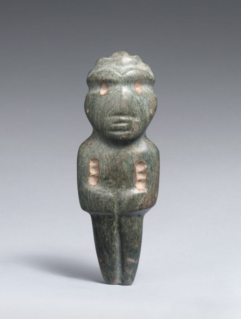 Standing stone figure with pecked round eyes, humanistic facial features, and arms folded across the abdomen.