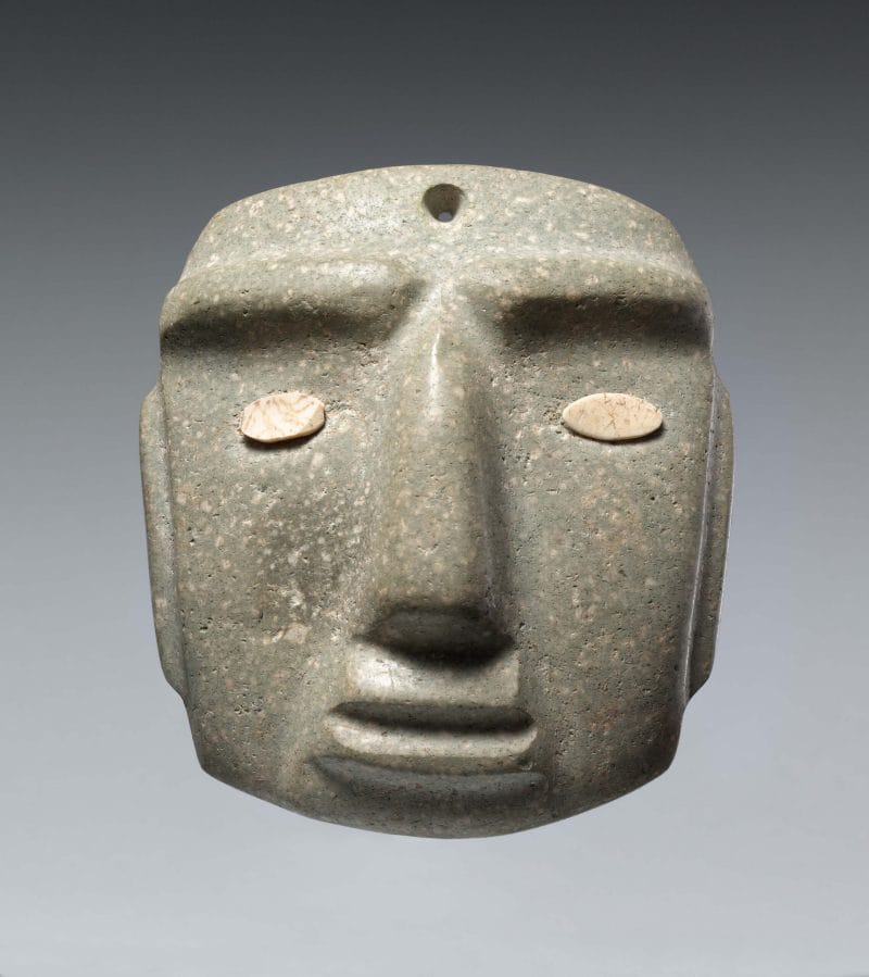 A stone mask with indented facial features and inlaid shell to represent the eyes.