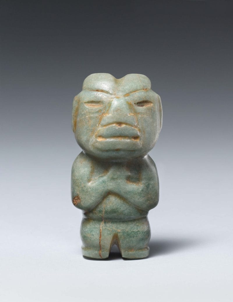 Standing stone figure of a man with stylized geometric facial features, almond-shaped eyes and rounded body parts.