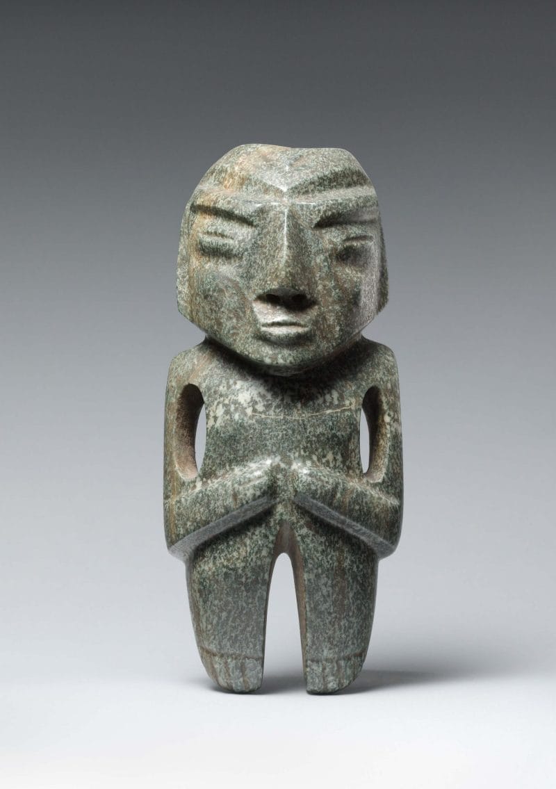 Small abstract stone figure with indented facial features features, a large pointed nose, and arms resting on its mid-section.