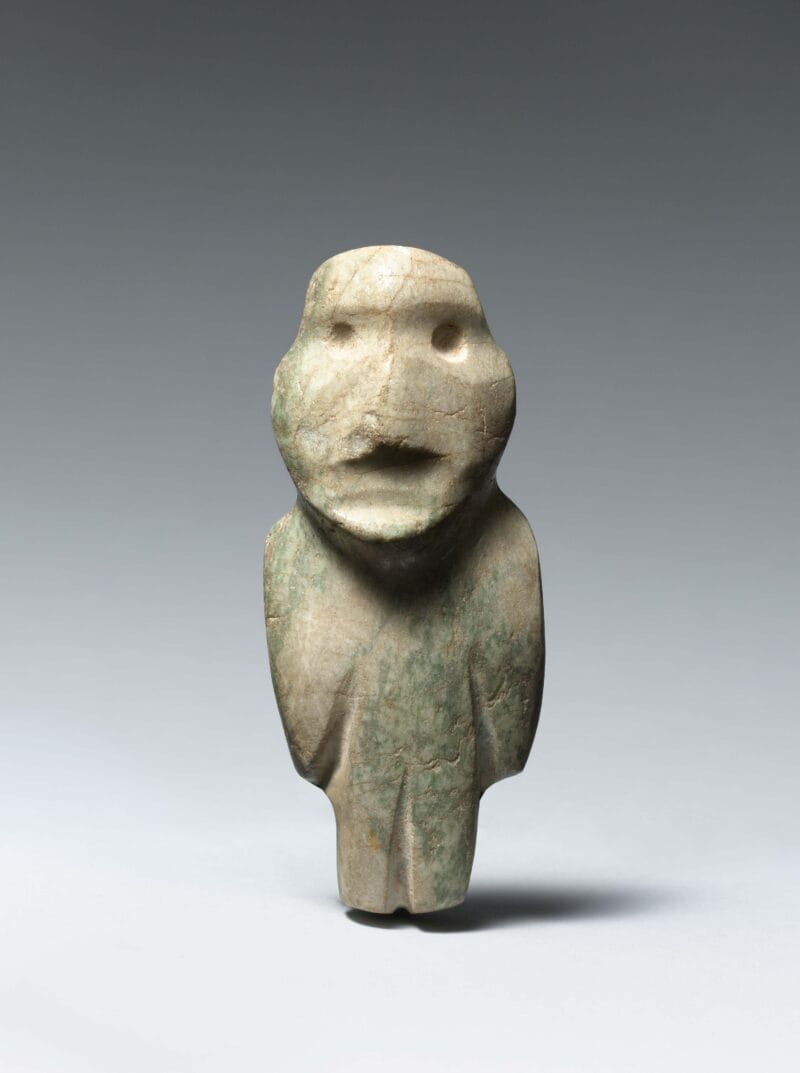 Standing abstract figure with large head, small drilled eyes, and barely carved out arms, and legs.