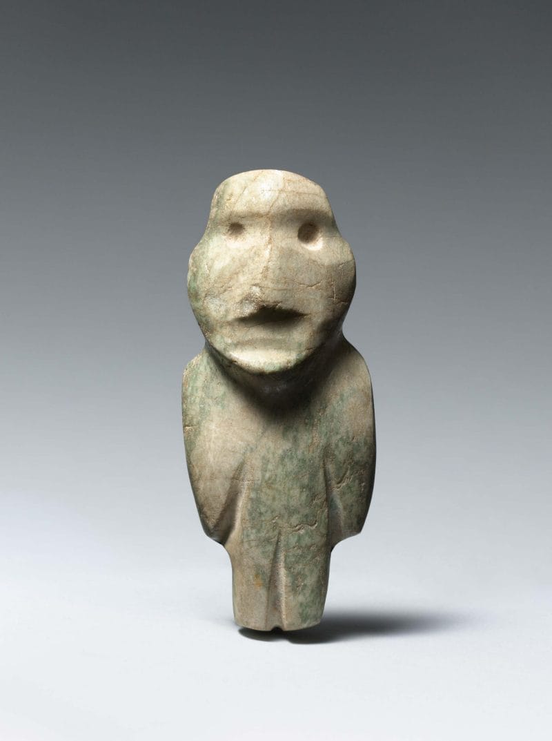 Standing abstract figure with large head, small drilled eyes, and barely carved out arms, and legs.