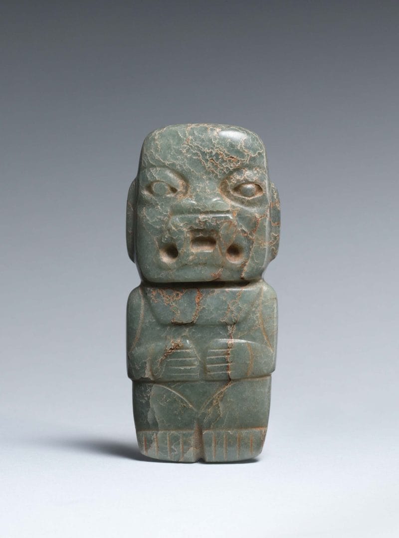 Male figure with almond-shaped eyes, cuts indicating arms, hands resting on knees across the torso, and a large open mouth with fangs.