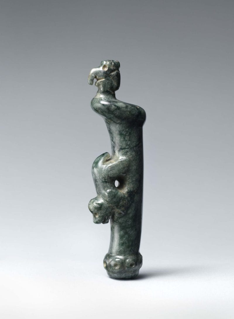 A long vertical pendant with a canine figure at the center of the celt and an avian effigy emerging at the top.