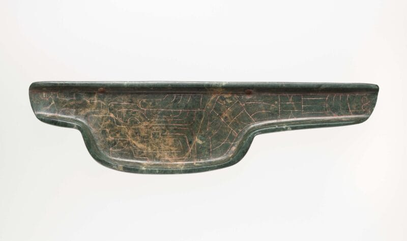 Flat, dark green celt with engraved imagery.