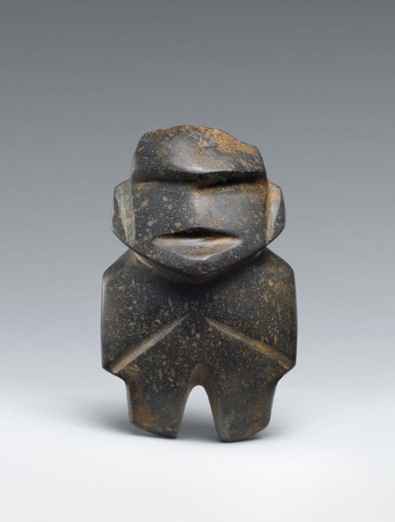 Abstract stone figure with vertical cuts to represent facial features, arms, legs, and prominent eyebrows.