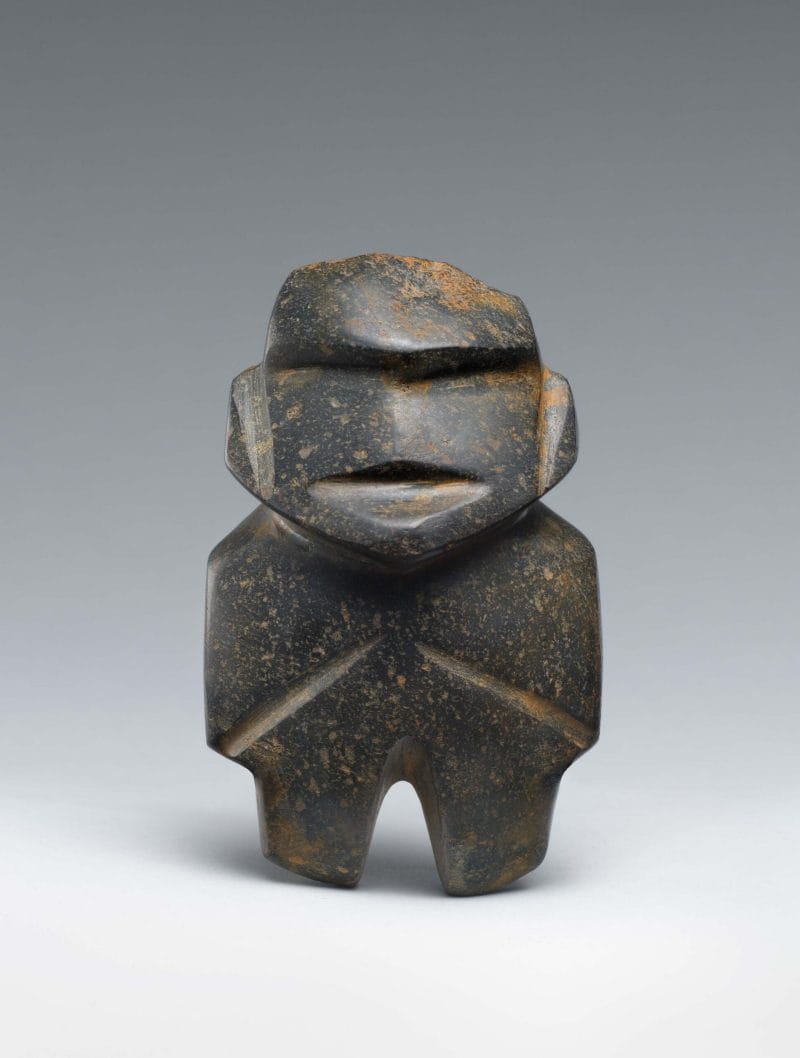 Abstract stone figure with vertical cuts to represent facial features, arms, legs, and prominent eyebrows.