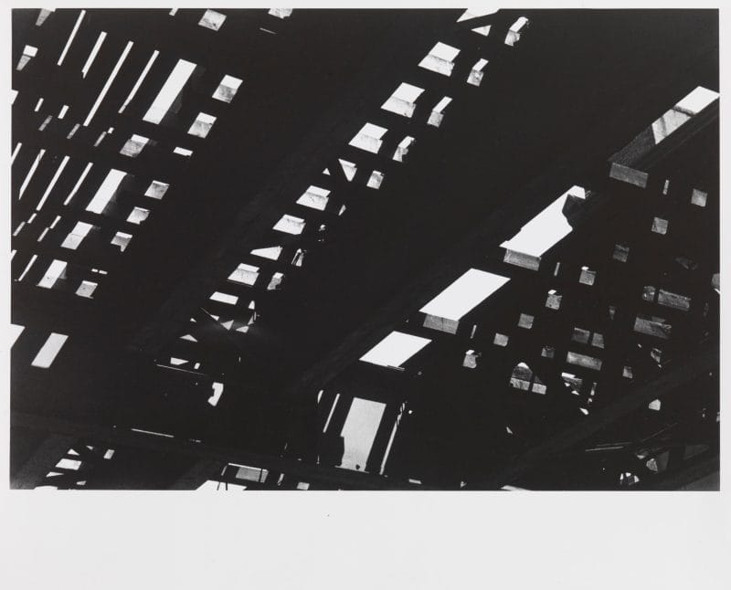 Black and white photograph of the view looking up at the underside of elevated train tracks.