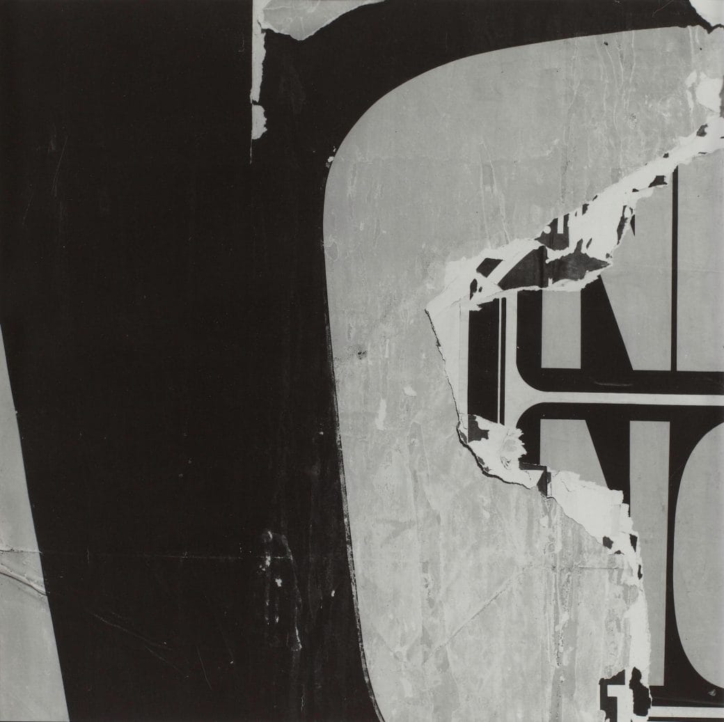 Black and white photograph of layered torn signs that reveal an obscured 'NO' present on the sign underneath.