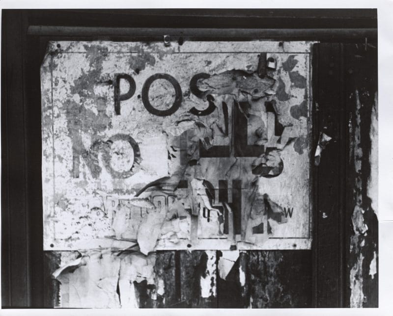 A black and white photograph of layered torn signs with the distinguishable words 
