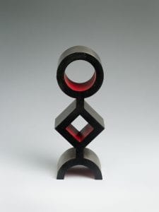 A black totem-like sculpture of a circle atop a diamond atop a half circle, with the inner lining painted red.