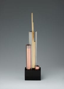 Vertical sculpture made up of a composite of steel, copper, and brass forms all extending upwards at varying lengths.