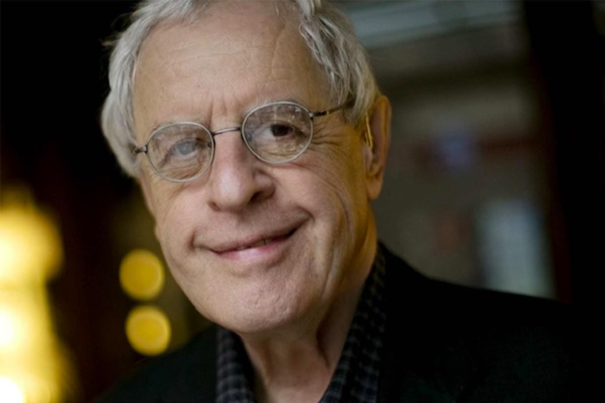 A photo of Charles Simic wearing a dress shirt and jacket at night outdoors.