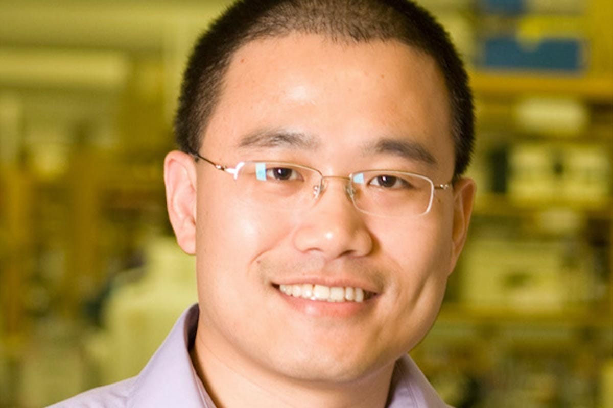 A photo of Yibin Kang in a yellow-lit science lab.