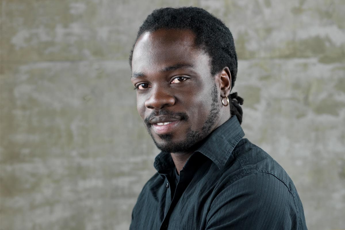 A photo of Michel Kouakou, wearing a black dress shirt, in a studio