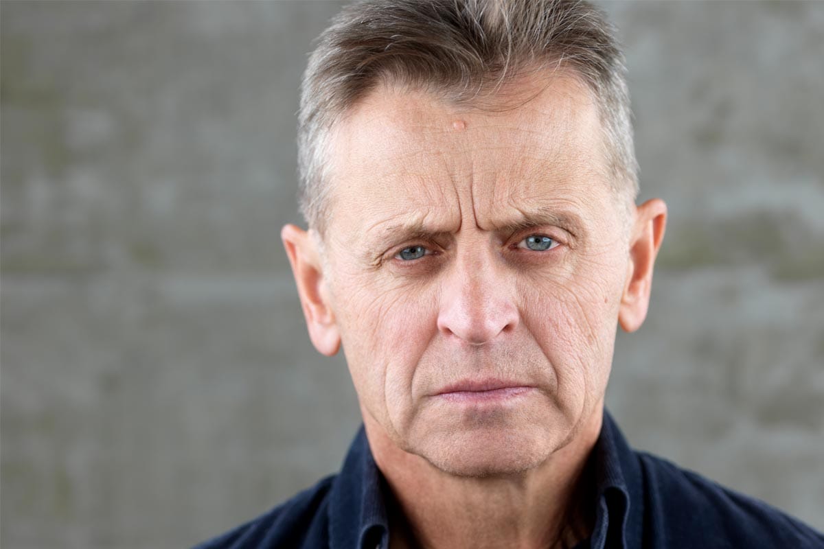 A photo of Mikhail Baryshnikov, wearing a blue dress shirt, in a studio.