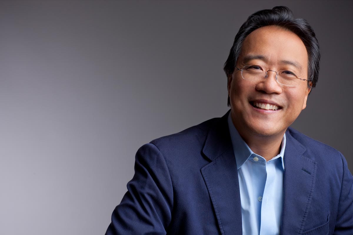 A photo of Yo-Yo Ma, wearing a blue dress shirt and jacket, against a gray neutral background.