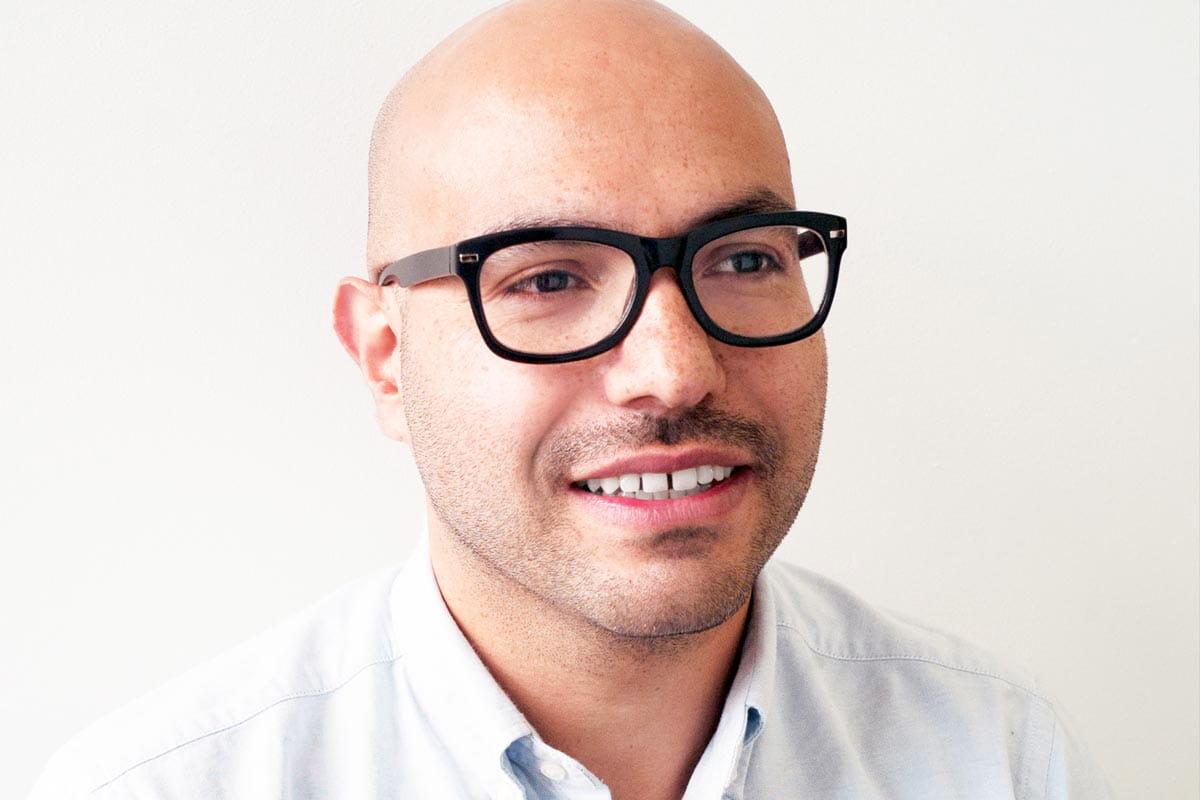 A portrait of Quilian Riano wearing a dress shirt against a white neutral background.