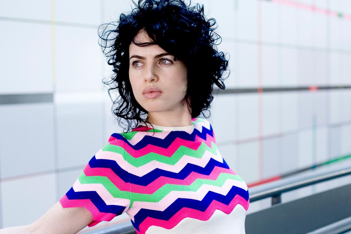 Neri Oxman in a striped blue, pink, green, and white shirt, looking away from the camera.