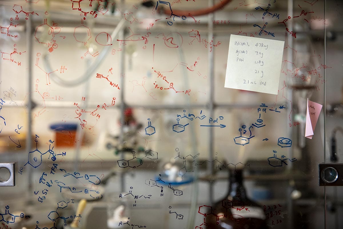 Scientific equations written in dry erase marker on a window of a chemistry lab bench.